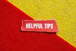 Helpful tips message written on ripped torn red paper piece with yellow red background. Conceptual helpful tips symbol. Copy space. photo