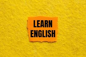 Learn english message written on ripped torn orange paper piece with yellow background. Conceptual learn english symbol. Copy space. photo
