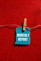 Monthly report message written on ripped torn blue paper piece with red background. Conceptual monthly report symbol. Copy space. photo