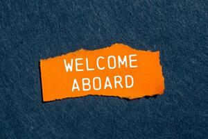 Welcome aboard message written on ripped torn orange paper piece with gray felt background. Conceptual welcome aboard symbol. Copy space. photo