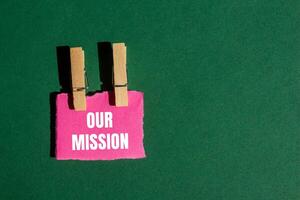 Our mission message written on ripped torn pink paper piece with green background. Conceptual our mission symbol. Copy space. photo