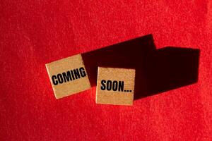 Coming soon message written on wooden cubes with red background. Conceptual coming soon symbol. Copy space. photo