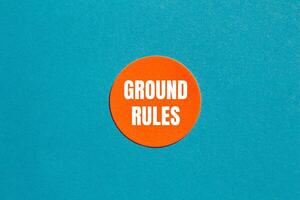 Ground rules message written on round orange sticker with blue background. Conceptual ground rules symbol. Copy space. photo