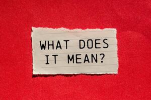 What does it mean question written on ripped torn paper piece on red background. Conceptual what does it mean question symbol. Copy space. photo