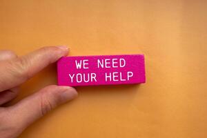 We need your help message written on pink wooden block with orange background. Conceptual we need your help symbol. Copy space. photo