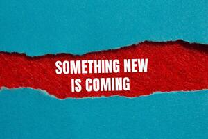 Something new is coming message written on ripped torn blue paper on red background. Conceptual something new is coming symbol. Copy space. photo