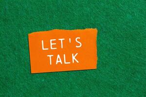 Let's talk message written on ripped orange torn paper piece on green background. Conceptual let's talk symbol. Copy space. photo