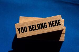 You belong here message written on wooden blocks on blue background. Conceptual you belong here symbol. Copy space. photo