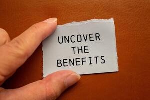 Uncover the benefits message written on ripped torn paper piece on brown background. Conceptual uncover the benefits symbol. Copy space. photo