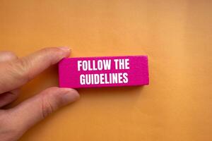 Follow the guidelines message written on pink wooden block with orange background. Conceptual follow the guidelines symbol. Copy space. photo