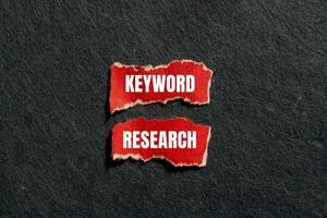 Keyword research message written on ripped torn red paper pieces with gray background. Conceptual keyword research symbol. Copy space. photo