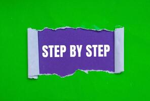 Step by step message written on ripped torn green paper on purple background. Conceptual step by step symbol. Copy space. photo