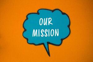 Our mission message written on blue paper speech bubble with orange background. Conceptual our mission symbol. Copy space. photo