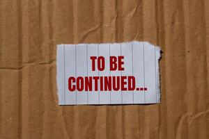 To be continued message written on ripped torn paper with cardboard background. Conceptual to be continued symbol. Copy space. photo