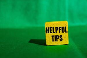 Helpful tips message written on yellow wooden cube with green background. Conceptual helpful tips symbol. Copy space. photo