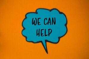 We can help message written on blue paper speech bubble with orange background. Conceptual we can help symbol. Copy space. photo