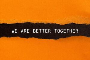 We are better together message written on ripped torn orange paper on black background. Conceptual we are better together symbol. Copy space. photo