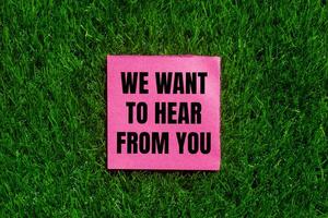 We want to hear from you message written on ripped torn pink paper with green grass background. Conceptual we want to hear from you symbol. Copy space. photo