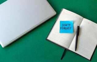 sticker reminder don't forget in notebook, laptop keyboard and open notebook on beautiful green background photo