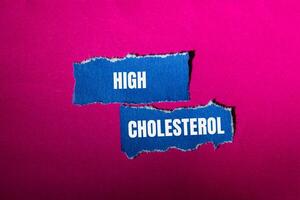 High cholesterol message written on ripped torn blue paper pieces with pink background. Conceptual high cholesterol symbol. Copy space. photo