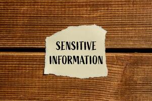 Sensitive information message written on ripped torn paper with wooden background. Conceptual sensitive information symbol. Copy space. photo