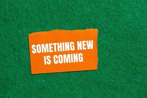Something new is coming message written on ripped orange torn paper piece on green background. Conceptual something new is coming symbol. Copy space. photo