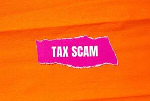 Tax scam message written on ripped torn pink paper with orange background. Conceptual tax scam symbol. Copy space. photo