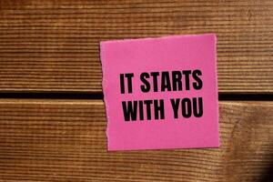 It starts with you message written on ripped torn pink paper piece with wooden background. Conceptual it starts with you symbol. Copy space. photo