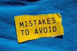 Mistakes to avoid message written on ripped torn yellow paper piece with blue background. Conceptual mistakes to avoid symbol. Copy space. photo