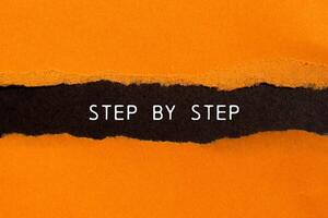 Step by step message written on ripped torn orange paper on black background. Conceptual step by step symbol. Copy space. photo