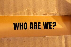 Who are we question written on ripped torn cardboard paper with orange background. Conceptual who are we question symbol. Copy space. photo