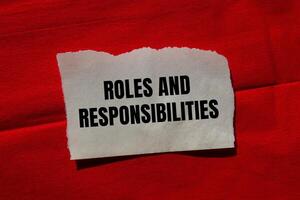 Roles and responsibilities message written on ripped torn paper piece on red background. Conceptual roles and responsibilities symbol. Copy space. photo
