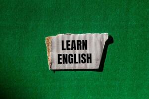 Learn english message written on ripped torn white paper piece with green background. Conceptual learn english symbol. Copy space. photo