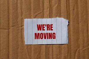 We are moving message written on ripped torn paper with cardboard background. Conceptual we are moving symbol. Copy space. photo