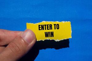 Enter to win message written on ripped torn yellow paper with blue background. Conceptual enter to win symbol. Copy space. photo
