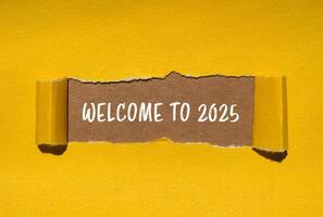 Welcome to 2025 message written on ripped torn yellow paper with brown background. Conceptual welcome to 2025 symbol. Copy space. photo