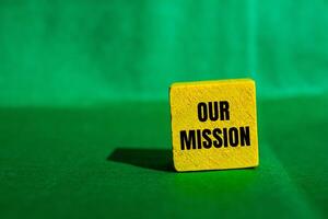 Our mission message written on yellow wooden cube with green background. Conceptual our mission symbol. Copy space. photo