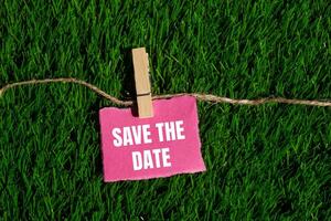 Save the date message written on ripped torn pink paper piece with green grass background. Conceptual save the date symbol. Copy space. photo