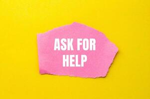 Ask for help message written on ripped torn pink paper piece with yellow background. Conceptual ask for help symbol. Copy space. photo
