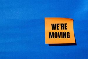We are moving message written on orange paper with blue background. Conceptual we are moving symbol. Copy space. photo