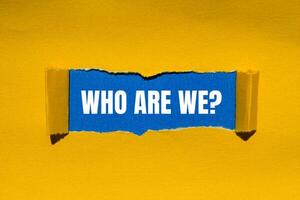 Who are we question message written on ripped torn yellow paper with blue background. Conceptual who are we question symbol. Copy space. photo