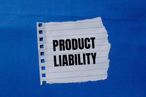 Product liability message written on ripped torn paper piece with blue background. Conceptual product liability symbol. Copy space. photo