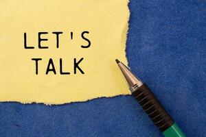 Let's talk message written on ripped torn yellow paper with a pen on blue background. Conceptual let's talk symbol. Copy space. photo