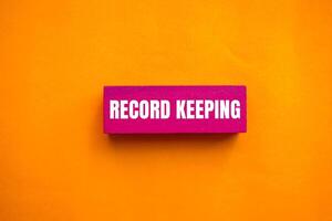 Record keeping message written on pink wooden block with orange background. Conceptual record keeping symbol. Copy space. photo
