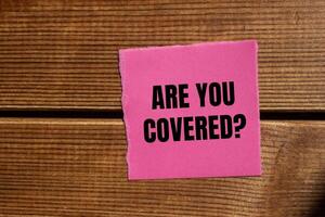 Are you covered question written on ripped torn pink paper piece with wooden background. Conceptual are you covered question symbol. Copy space. photo