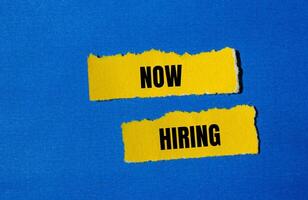 Now hiring message written on ripped yellow torn paper pieces with blue background. Conceptual now hiring symbol. Copy space. photo