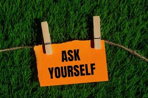 Ask yourself message written on ripped torn orange paper piece with green grass background. Conceptual ask yourself symbol. Copy space. photo