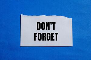 Don't forget message written on ripped white torn paper piece with blue background. Conceptual don't forget symbol. Copy space. photo