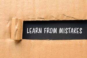 Learn from mistakes message written on ripped torn cardboard paper with black background. Conceptual learn from mistakes symbol. Copy space. photo