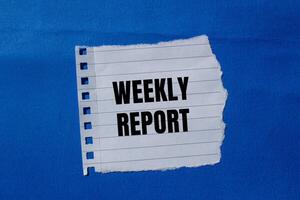 Weekly report message written on ripped torn paper piece with blue background. Conceptual weekly report symbol. Copy space. photo